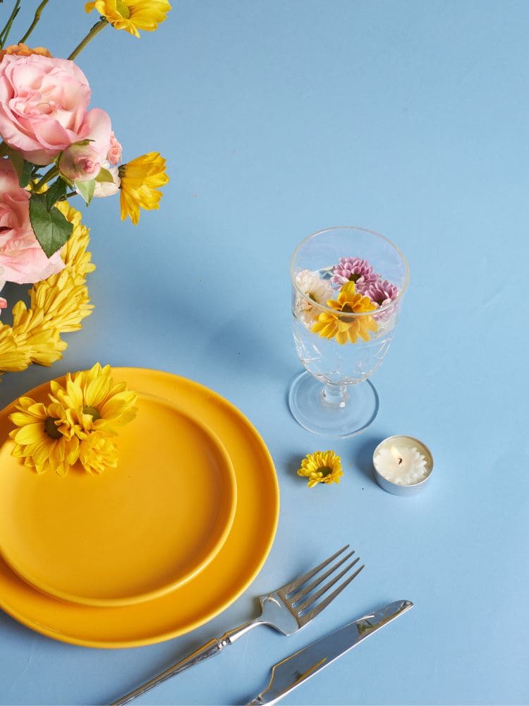 Mesa posta com pratos amarelos com flores de verão em volta 