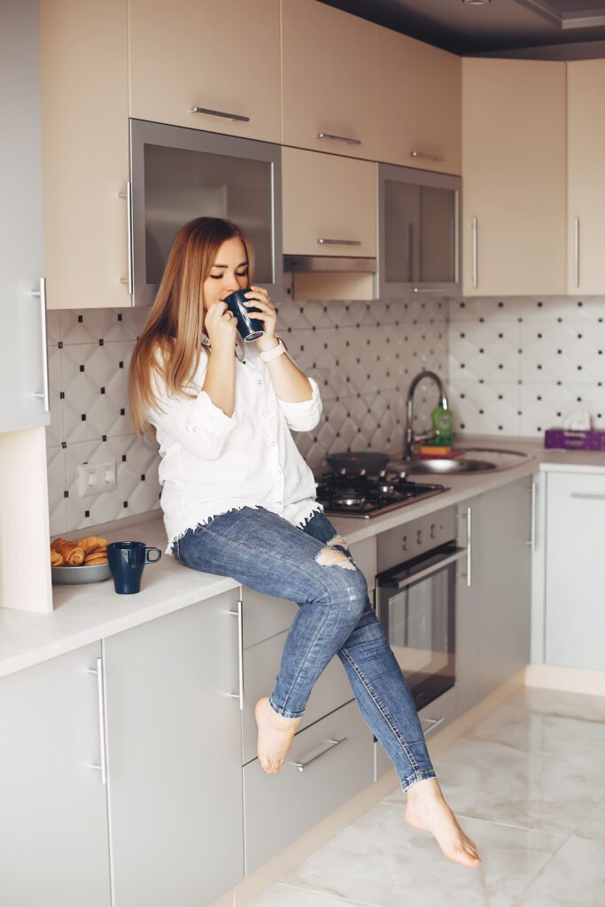 Jovem em cima da sua pia a vontade tomando café com o dia livre pela frente e moostra Como planejar uma cozinha pequena de apartamento